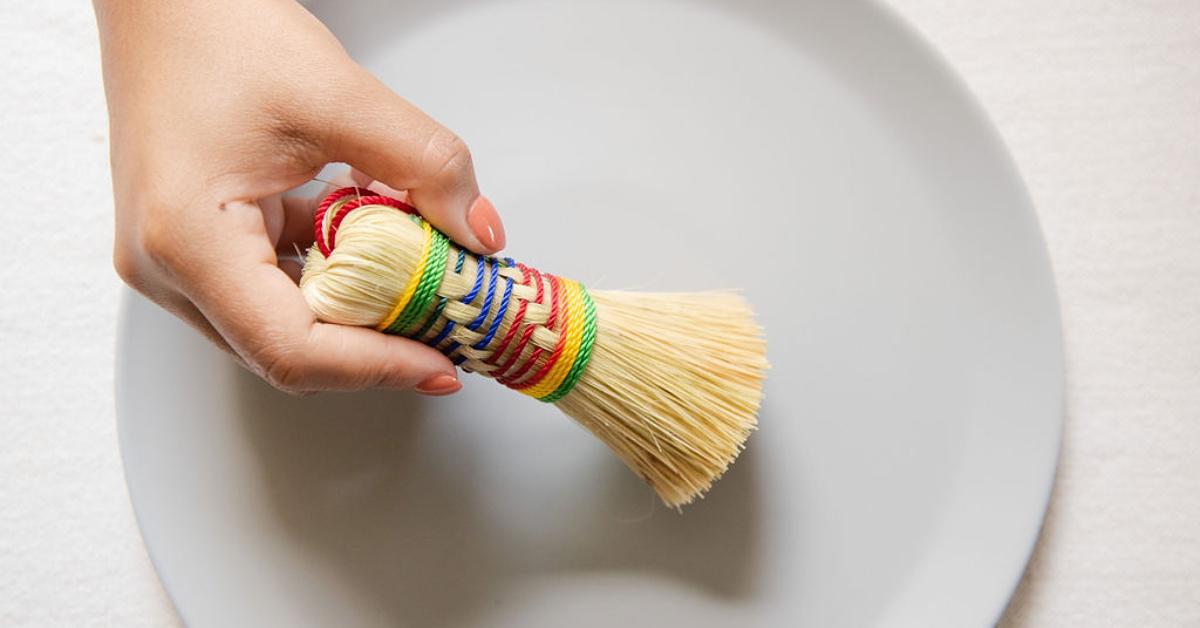 Photo of a hand holding an escobeta dish brush over a white dish